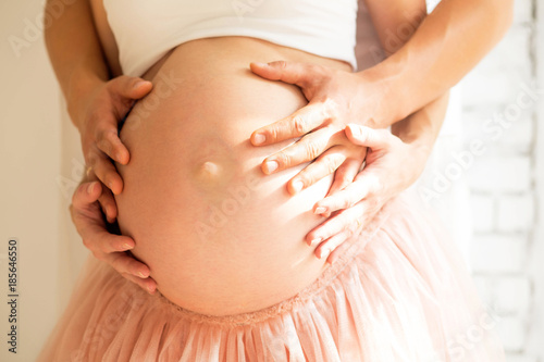 two pairs of hands on the bare belly of a pregnant woman