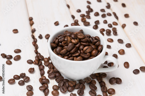 coffee beans in a white porcelain cup and scattered on a white wooden table