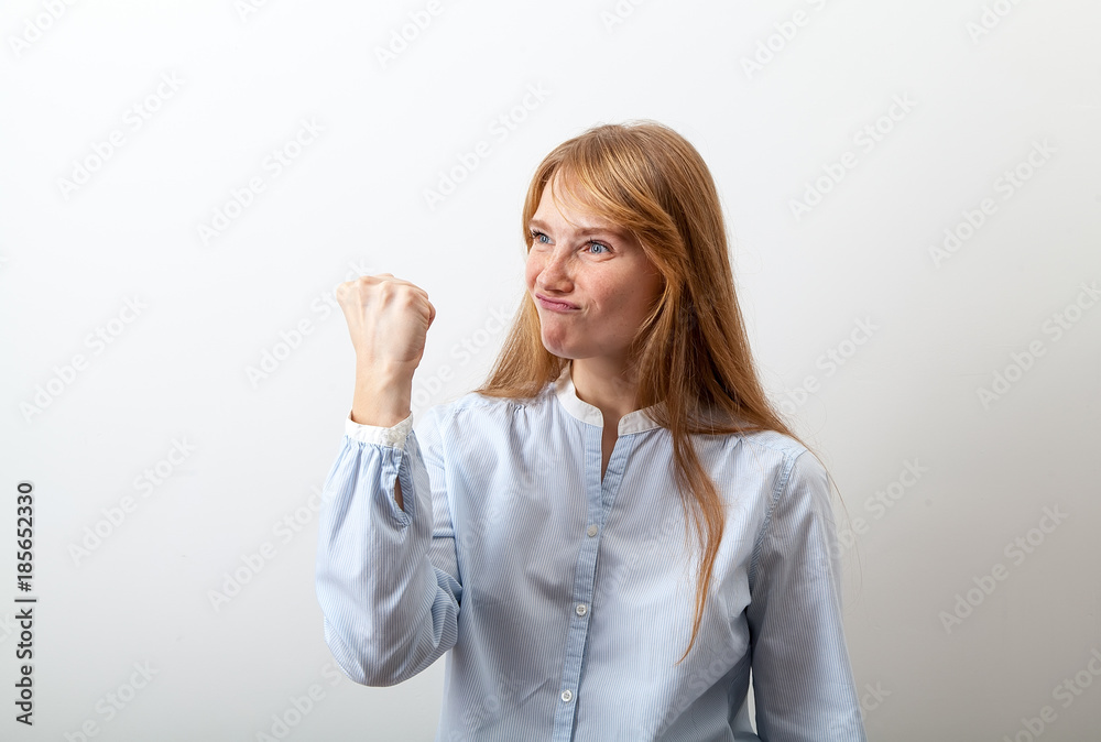 Portrait of young red-headed girl with white skin and freckles showing a feast to somebody with angry, but flirting expression. White background. Portrait of young red-headed girl with white skin and freckles showing a feast to somebody with angry, but flirting expression. White background.