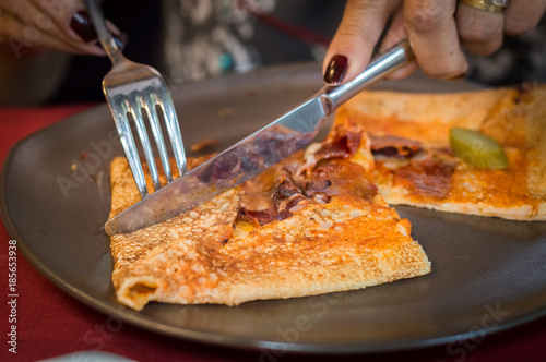 Woman hand cutting of a portion of delicious crepe with meat served on a grey plate.