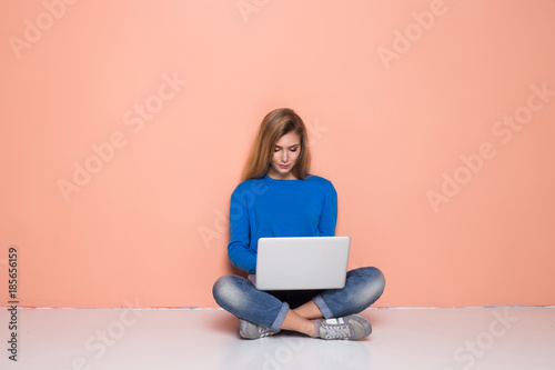 Serious woman working with laptop while sitting on floor isolated. Woman typing on laptop computer while sitting on the floor with legs crossed.