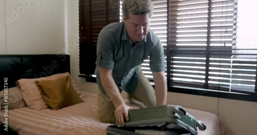 Man trying to close his travel bag drops it on the floor while packing photo