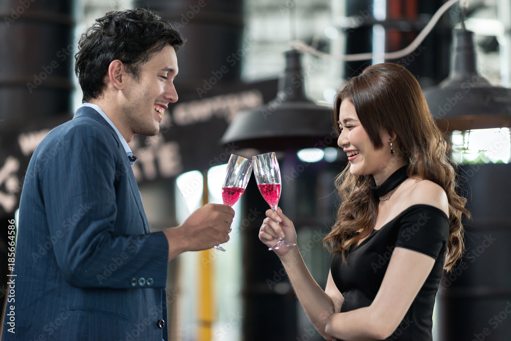 Portrait of smiling young man and woman talking while holding red sparkling wine glass. Pretty single girl flirting with young handsome man in a real bar scene, trying to take her home. Party concept.