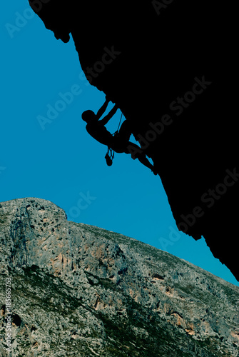Silhouette of a climber on an overhanging rock against the backdrop of a rocky island