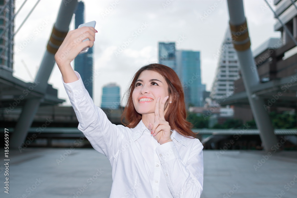 Fototapeta premium Pretty face young Asian woman taking a selfie photo at urban city background. Selective focus and shallow depth of field.