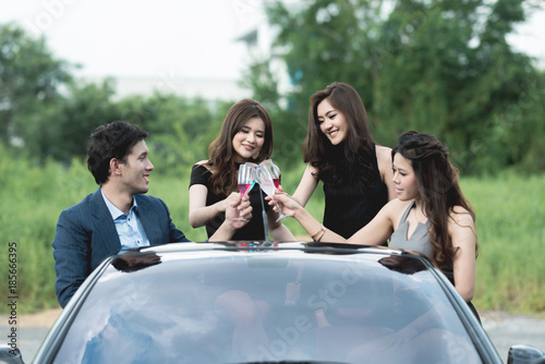 Playboy party concept. Young white male inside convertible sport car with three beautiful asian women doing a champagne toast before going to a carefree party.