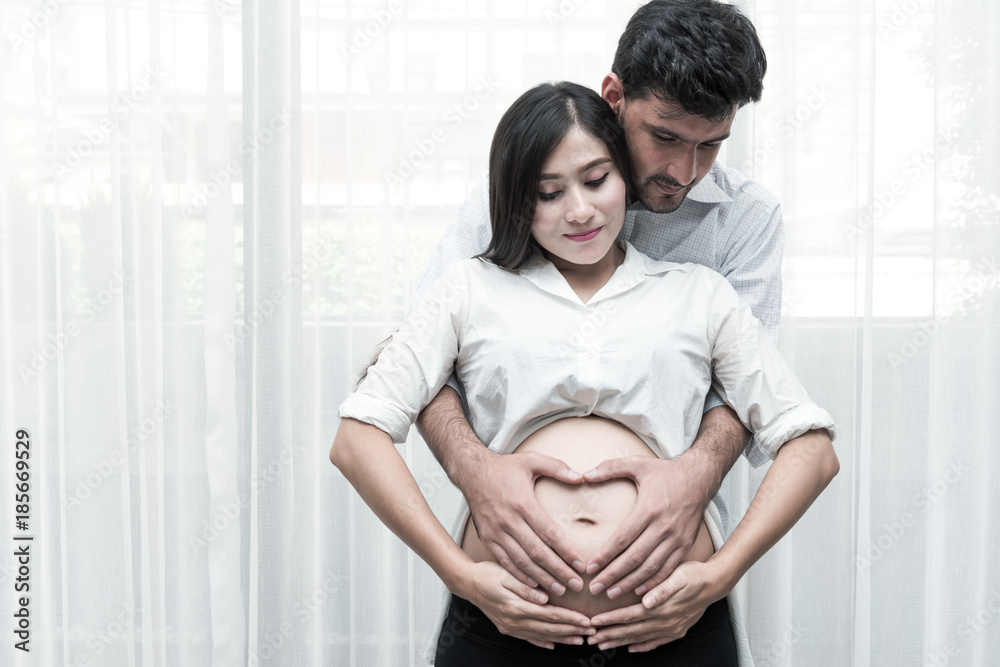 Mixed race parenthood concept. Portrait of young Chinese pregnant and her white male husband holding each other. Taken indoor with real six months old pregnant woman. Mixed race parenthood concept. Portrait of young Chinese pregnant and her white male husband holding each other. Taken indoor with real six months old pregnant woman.