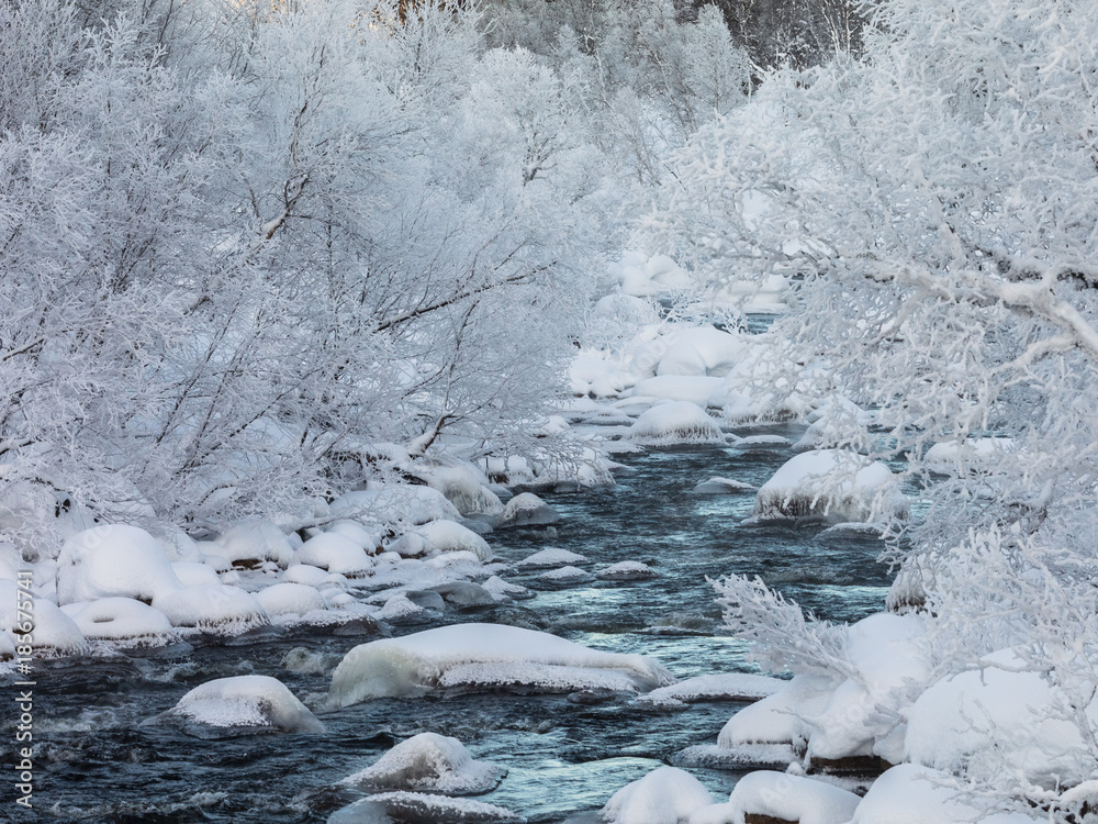 A streaming winter creek, snow and ice, river surrounded with snow covered trees