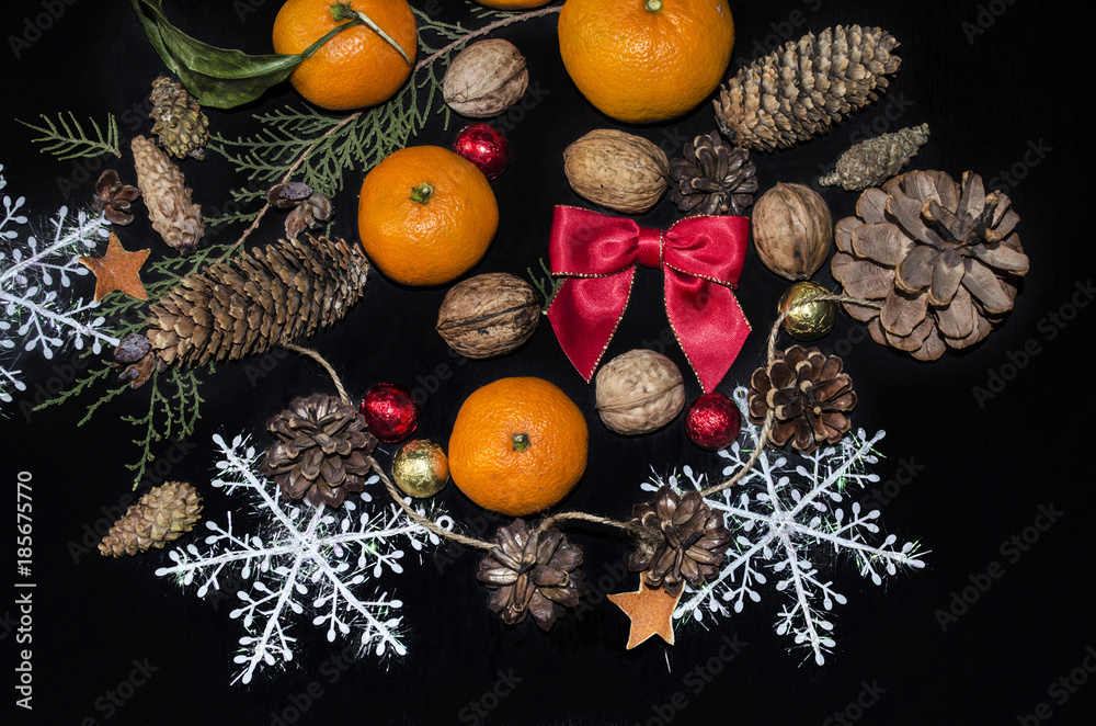 Red satin bow and tangerines with a sprig of cypress,pine cones,nuts,chocolate balls with snowflakes on a black plywood