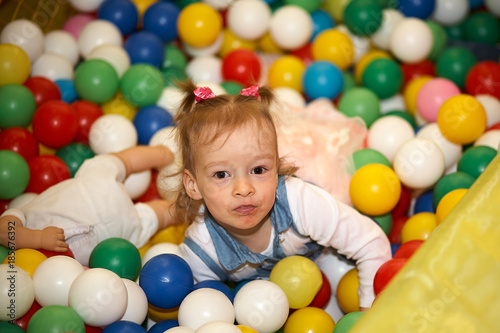 Happy little kid girl play in the playing room pool full of colorful balls. Funny child having fun indoors. Birthday party