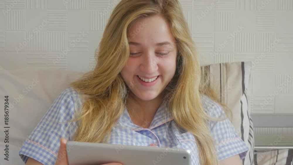 Beautiful happy smiling blond woman in bed using her tablet to watch comedy Beautiful happy smiling blond woman in bed using her tablet to watch comedy