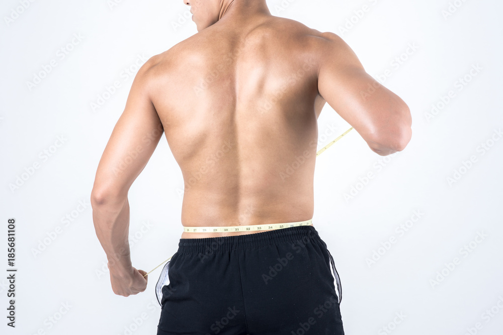 Fitness and health concept. Fit sport man measuring waist to check his body fat amount, isolated on white background. Half naked Asian chinese lean muscular male wearing a black shorts.