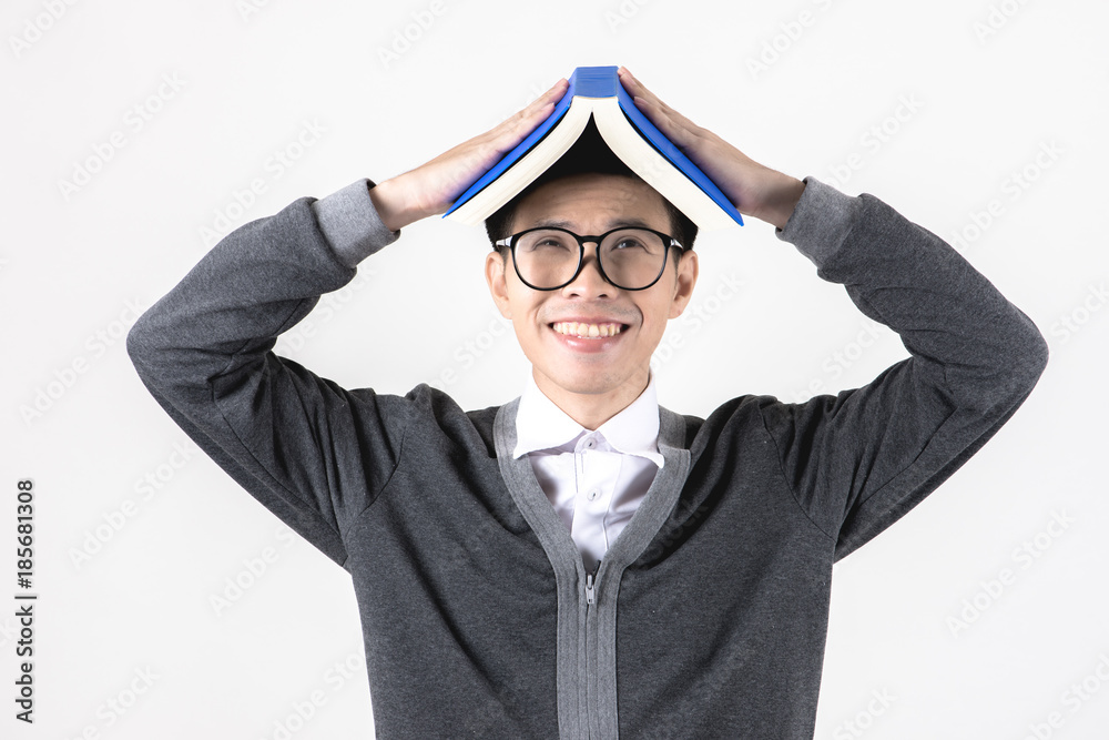 Nerd studying hard. Young Asian nerd man wearing glasses holding text book on his head standing isolated on white background. Black hair, grey sweater, white shirt. Education concept. Nerd studying hard. Young Asian nerd man wearing glasses holding text book on his head standing isolated on white background. Black hair, grey sweater, white shirt. Education concept.