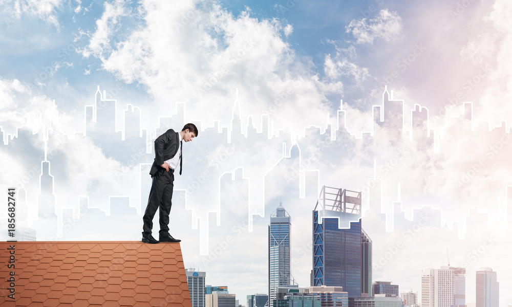 Businessman looking down from roof and modern cityscape at background. Mixed media