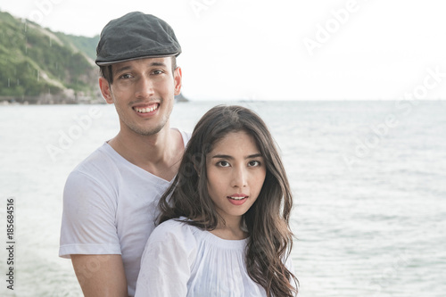 Couple holding each other on beach. Young happy interracial couple on beach holding each other. Asian woman, Caucasian man. Young mixed race romance concept.