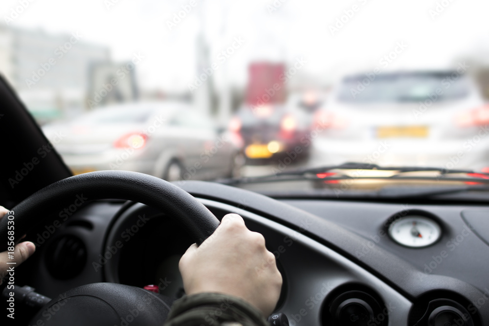 female caucasian hands holding the steering wheel of a car while stuck in a traffic jam