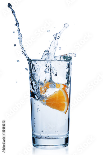 Slice orange dropping into water glass on white background