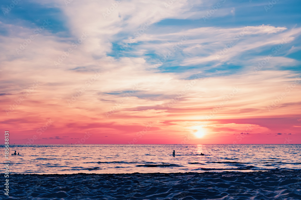 Coast of the sea at colorful sunset, Koh Chang, Thailand. Silhouette of swimming people visible in water. Evening calm on the Gulf of Thailand. Bright afterglow.