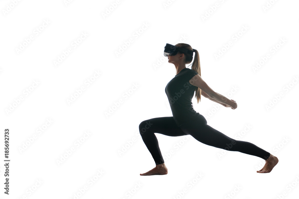 A young beautiful girl in virtual reality glasses makes yoga and aerobics remotely. Future technology concept. Modern imaging technology. Classes in single sports remotely. On a white background