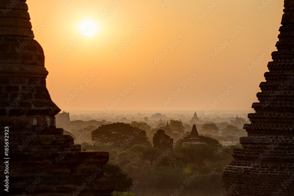 Silhouette of many pagodas and temples and sunrise over misty plain in Bagan, Myanmar (Burma), viewed slightly from above.