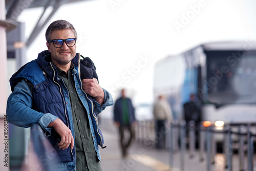 Holiday time. Portrait of pleasant middle-aged man in glasses is looking at camera with joy. He is standing outdoors while carrying his backpack. Copy space in the right side © Yakobchuk Olena