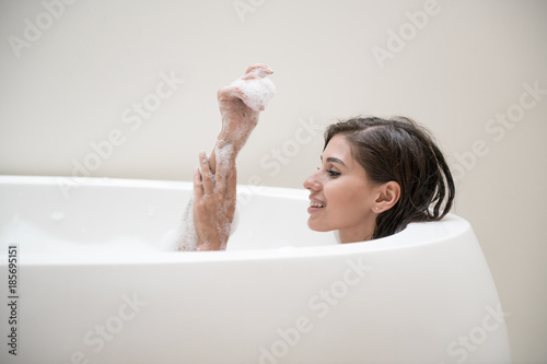 Beautiful young white woman enjoy relaxing in bubble bath. Resting, relaxing, touhing her arm, smiling. White caucasian woman. photo