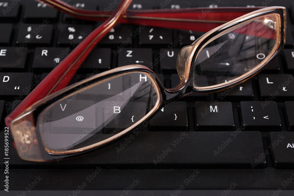 Black computer keyboard and glasses, close up. Selective focus.
