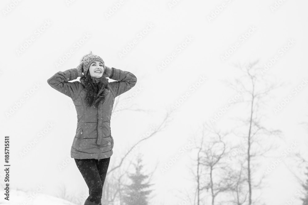 Fototapeta premium Young woman walking in a nature park and breathing fresh winter air feeling wonderful at weekend. Young hipster girl wear blue coat and grey knitted hat in winter weather having fun outdoors