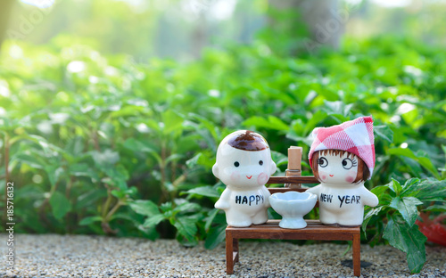New year concept idea with little ceramic of girl and boy dolls sitting on wooden chair with green background.