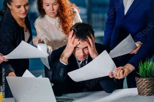 Businessman holding head with hands surrounded by worried colleagues with business documents in hands. missing dedline photo