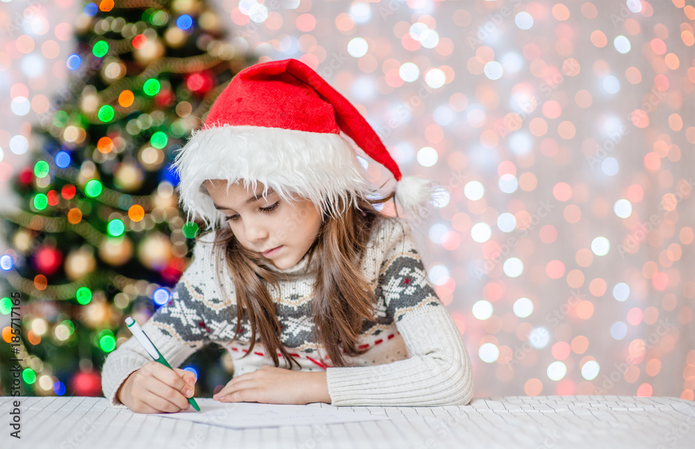 Happy little girl in red christmas hat writes letter to Santa Claus. Space for text Happy little girl in red christmas hat writes letter to Santa Claus. Space for text