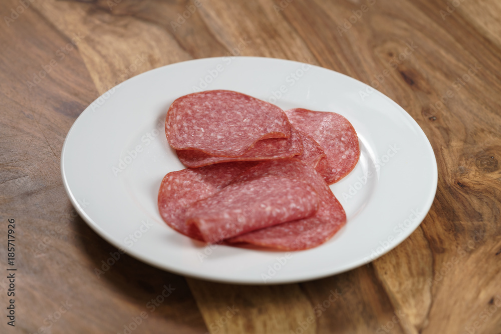 sliced salami on white plate on wood table