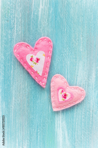 Valentine's Day concept with two handmade pink felt hearts on turquoise color wooden background