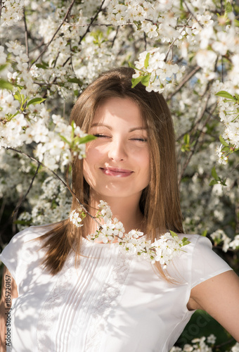 Vertical portrait of a young attractive woman in the flowered garden. Smile with your eyes closed