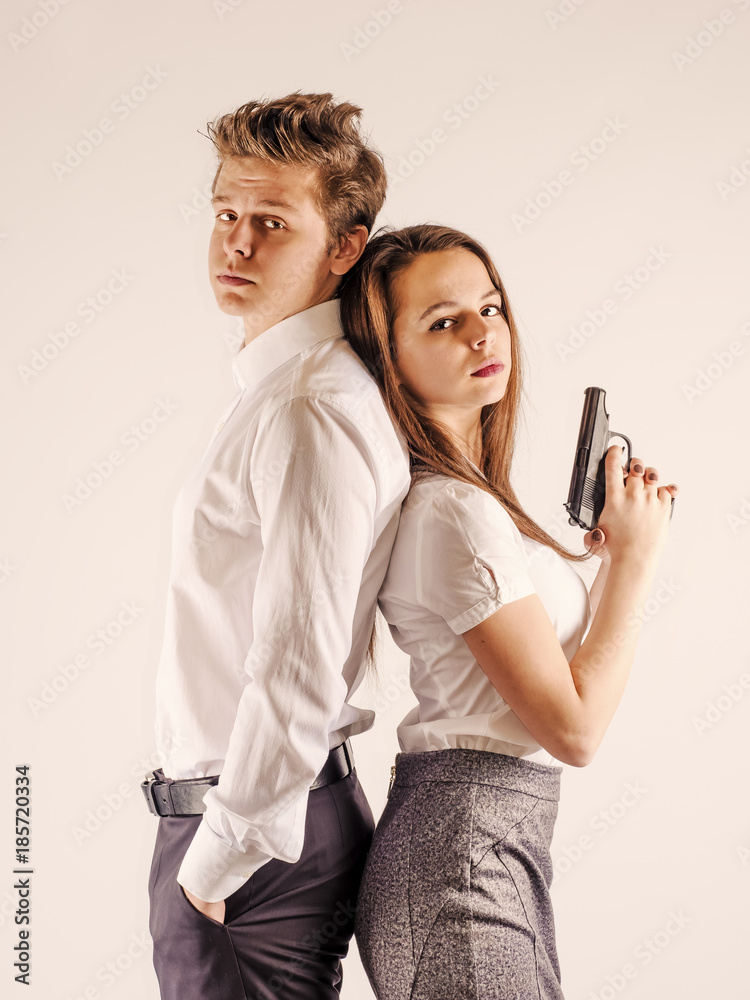 A cute guy and a girl are standing with a gun. Secret Service. White background. A cute guy and a girl are standing with a gun. Secret Service. White background.