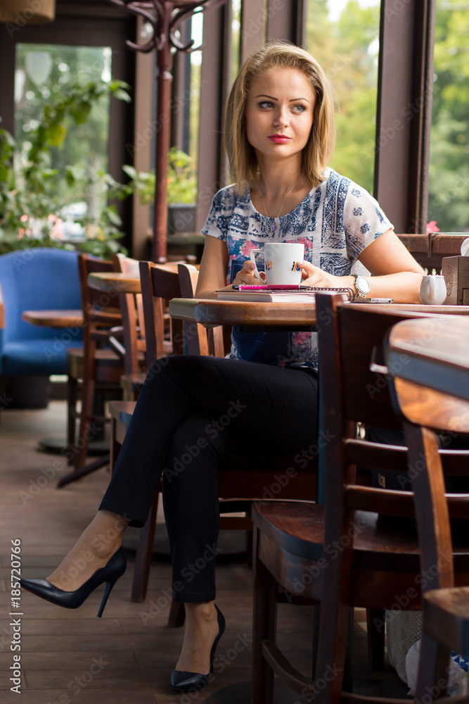 Young Business Woman in the Cafe with a Cup of Coffee and a Phone 