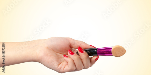 Woman hand with a foundation cosmetic tool isolated on color background