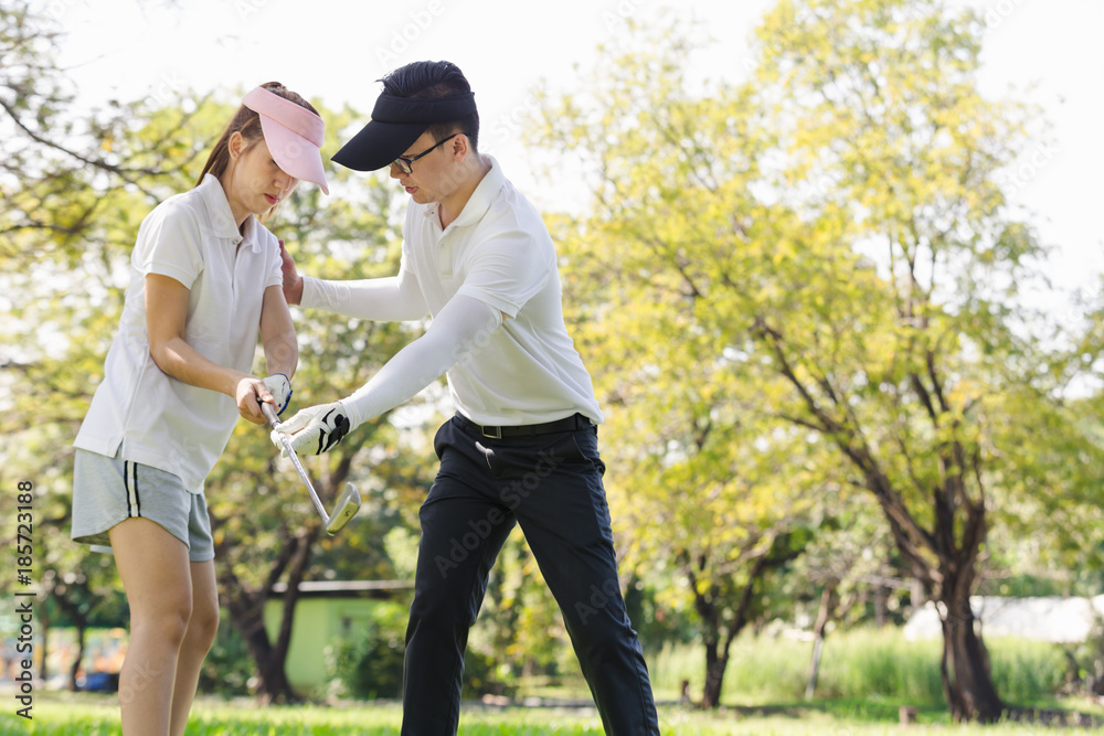 Asian couple playing golf. man teaching woman to play golf while standing on field