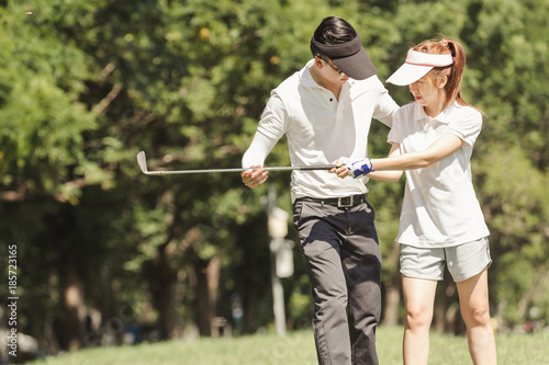 Asian couple playing golf. man teaching woman to play golf while standing on field