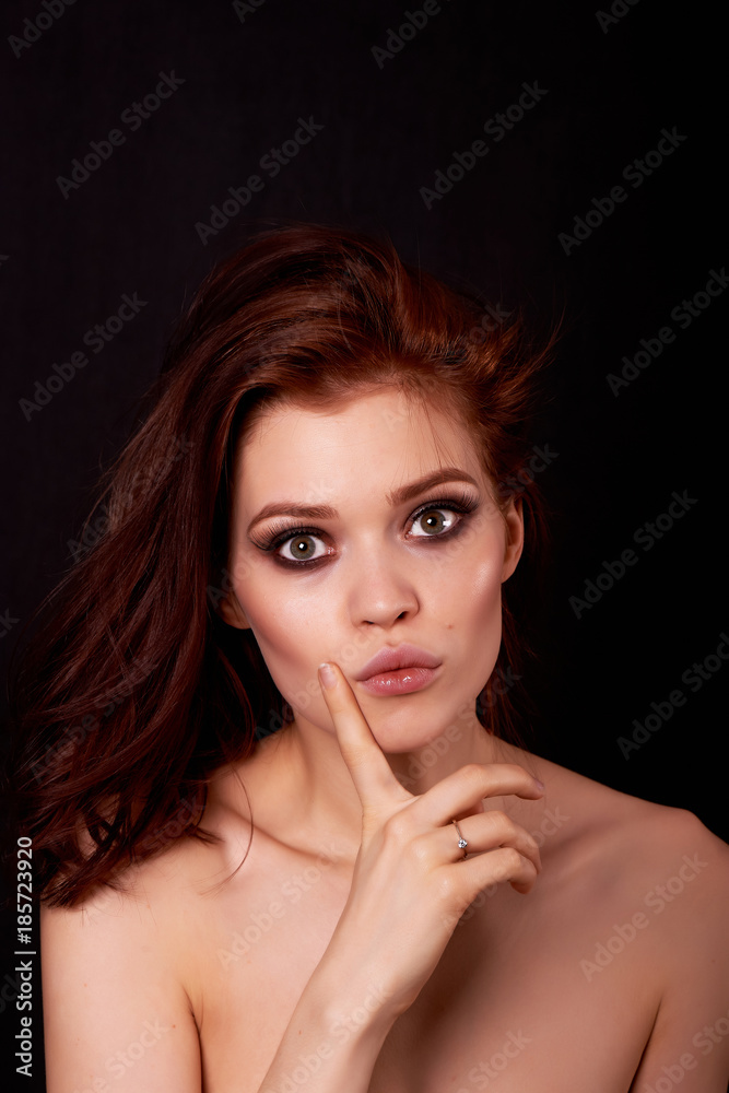 Beautiful redhead girl on a black background. In the eyes of surprise and question. Finger near the face. Emotions Beautiful redhead girl on a black background. In the eyes of surprise and question. Finger near the face. Emotions