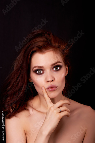 Beautiful redhead girl on a black background. In the eyes of surprise and question. Finger near the face. Emotions