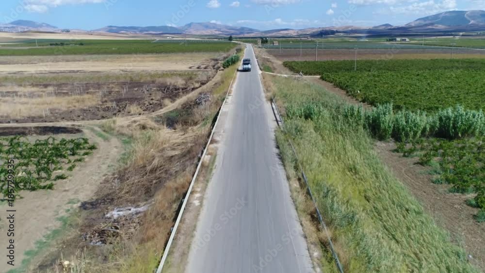 Low altitude aerial above rural road flying towards and just over truck driving in opposite way also showing the rural southern europe landscape and hills in background and some clouds 4k quality