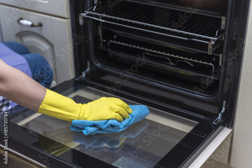Women's hand in protective gloves wipes the kitchen gas stove with a blue rag.