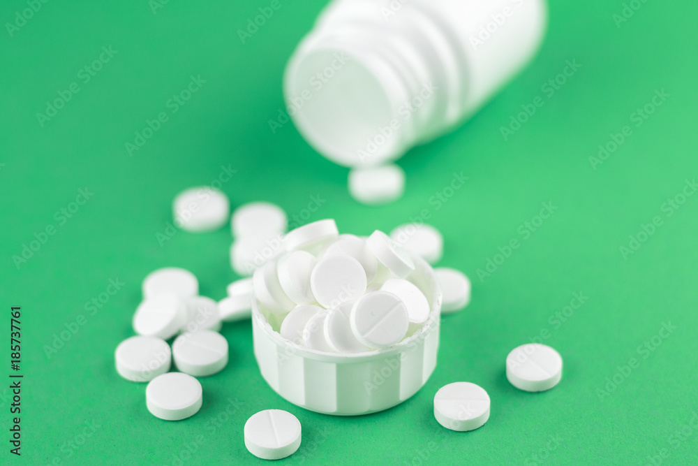 Close up white pill bottle with spilled out pills and capsules in cap on jade green background with copy space. Focus on foreground, soft bokeh. Pharmacy drugstore concept Close up white pill bottle with spilled out pills and capsules in cap on jade green background with copy space. Focus on foreground, soft bokeh. Pharmacy drugstore concept