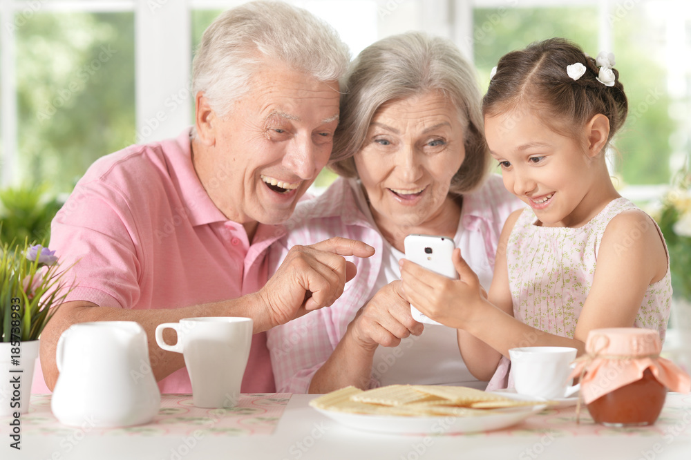 Smiling grandparents  with granddaughter using smartphone