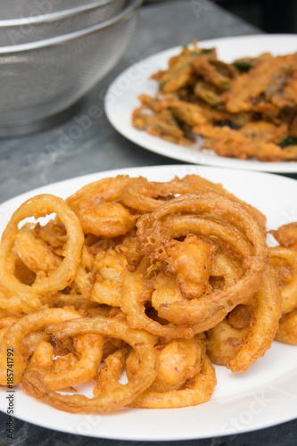 Onion ring in white dish with fried various vegetables on table