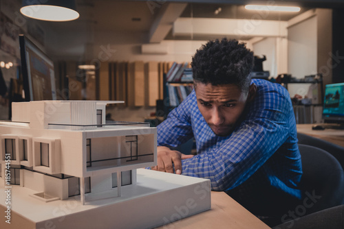 Young confident African American black male architect working on a private house project in the office, studying mansion model