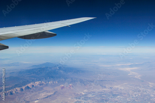 The view from a plane of the wing and the ground below with blue skies