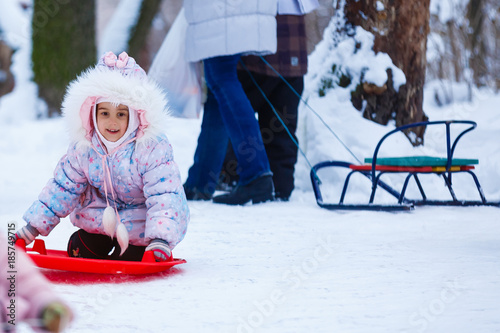 Little caucasian girl sledding, having fun on a sleigh ride at winter time. photo