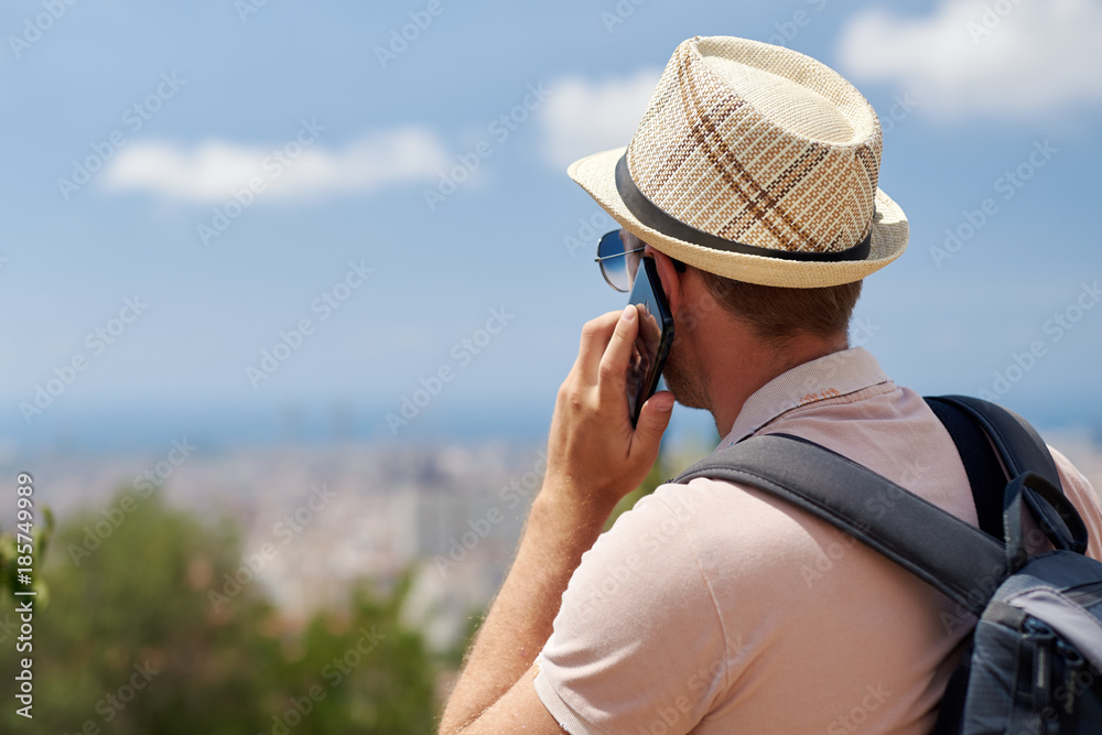 Male traveler in sunhat is talking on mobile phone.